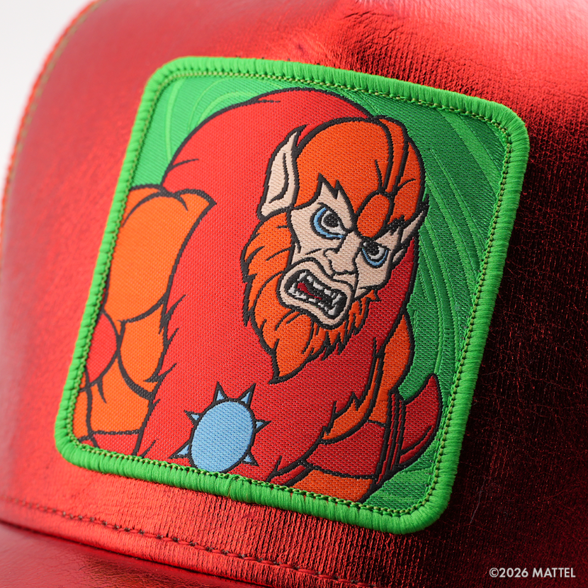 Woven patch of Beast Man from Masters of the Universe with an orange furry face and blue eyes, set against a leafy green background with green border, stitched onto the metallic red retro trucker cap.