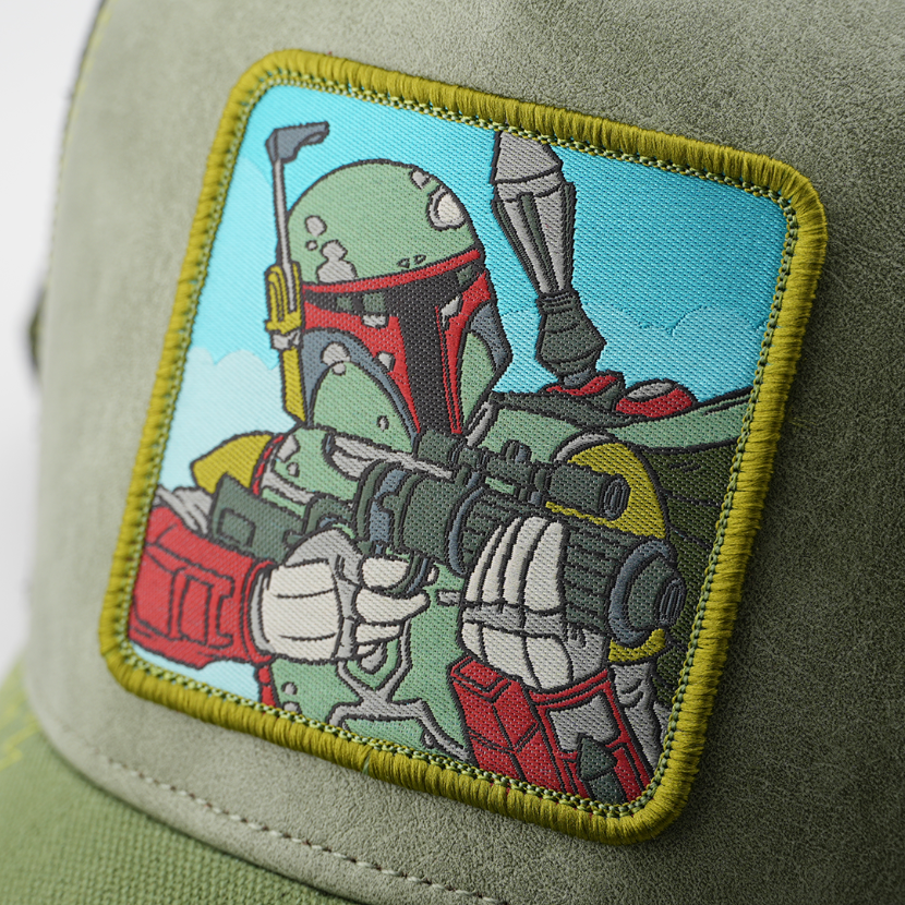 Close-up of the Boba Fett from Star Wars patch aiming his blaster against a sky background, stitched onto the green suede-texture trucker cap fabric.