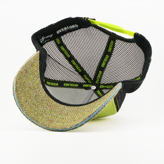 Underside of the Dr. Bunsen retro trucker cap, showing a tweed-textured brown brim, a Disney tag, gray mesh crown, and black Overlord branded taping with lime green text.