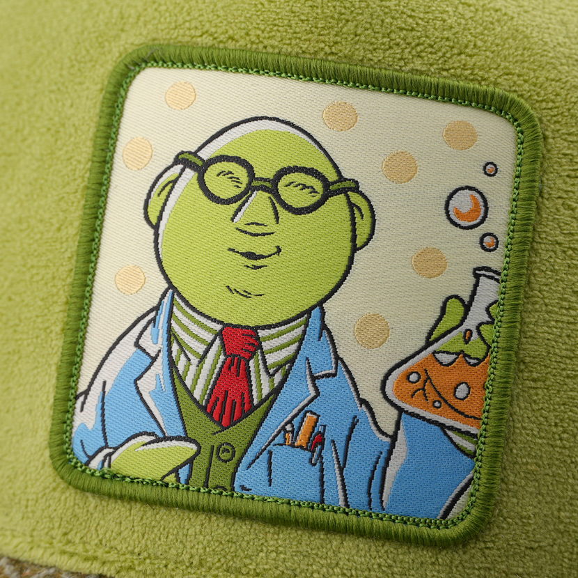 Close-up of a woven patch showing Dr. Bunsen from The Muppets in glasses and a lab coat holding a beaker with orange liquid on a polka-dot background, stitched onto suede-textured olive green fabric with a green border.