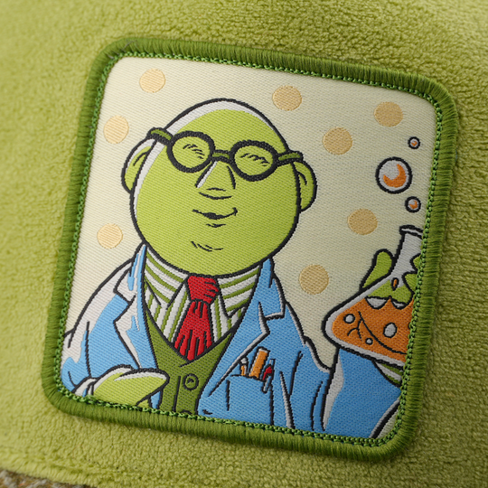 Close-up of a woven patch showing Dr. Bunsen from The Muppets in glasses and a lab coat holding a beaker with orange liquid on a polka-dot background, stitched onto suede-textured olive green fabric with a green border.