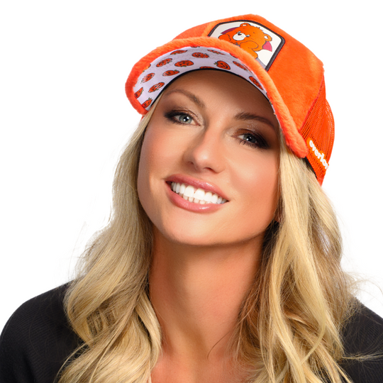 Woman wearing plush orange trucker cap hat featuring Trick or Sweet Bear from Care Bears on woven patch attached to crown