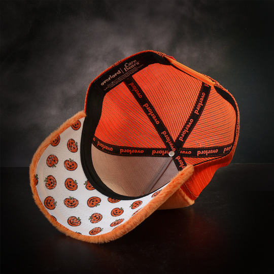 Inside view of plush orange trucker cap hat with jack o lantern pumpkins printed on the underbrim