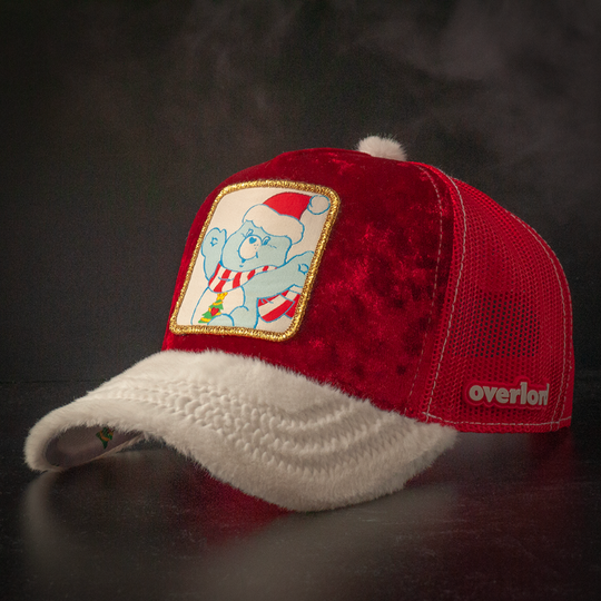 Red crushed velvet trucker cap with white faux fur brim and red mesh featuring a woven patch of Christmas Wishes Bear from Care Bears wearing a Santa hat and scarf attached to the crown.