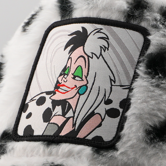 Close-up of Cruella de Vil from Disney's 101 Dalmatians patch against a swirling gray background, stitched onto the black and white faux-fur retro trucker cap fabric.