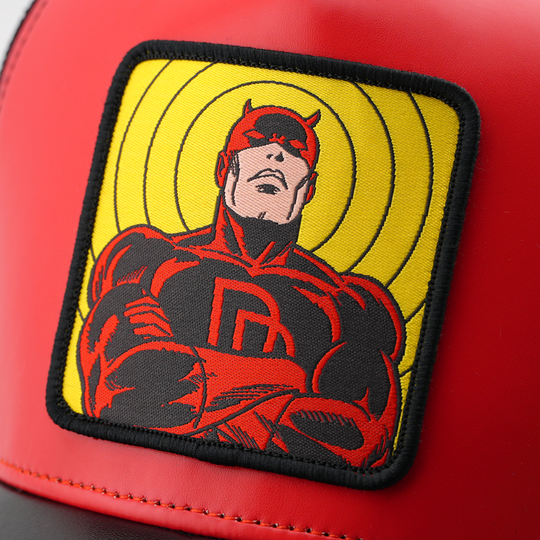 Close-up of a woven Marvel's Daredevil patch with radiating yellow rings, stitched onto matte red cap fabric.