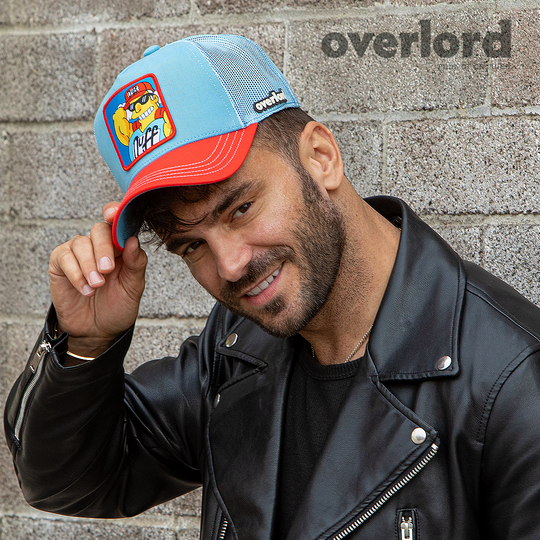Man wearing light blue and red OVERLORD X The Simpsons present smiling Duffman trucker baseball cap hat with light blue stitching. PVC Overlord logo.