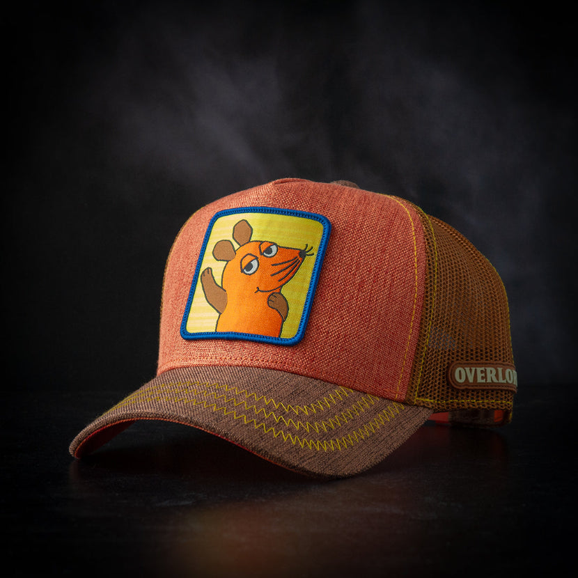 Orange and brown cap with a cartoon Die Maus patch on a dark background