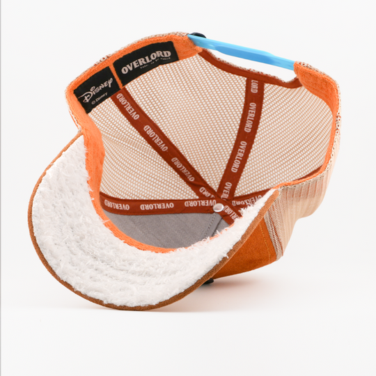 Underside of the Doc from Disney's Snow White and the Seven Dwarfs retro trucker cap showing a white fuzzy-textured brim, a Disney tag, tan mesh crown, and orange Overlord branded taping.