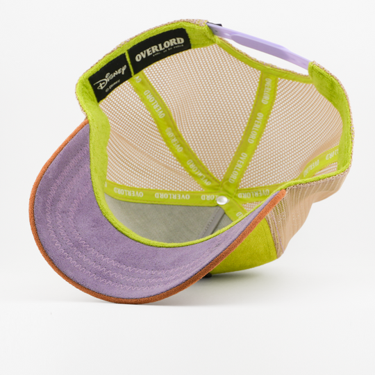 Underside of the Dopey from Disney's Snow White and the Seven Dwarfs retro trucker cap showing a plain purple suede-textured brim, a Disney tag, tan mesh crown, and green Overlord branded taping.