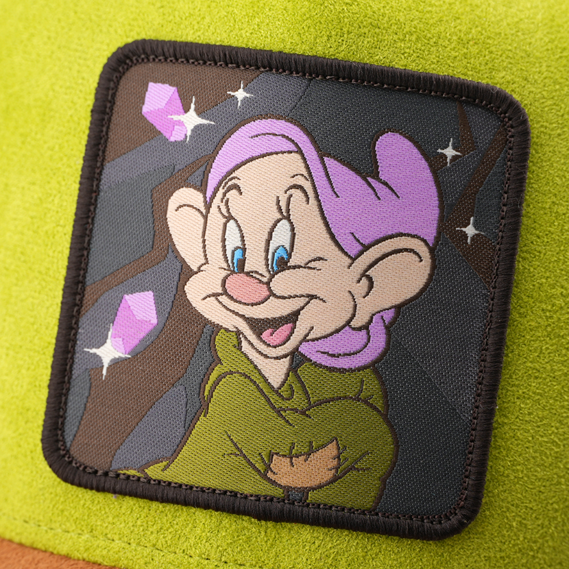 Woven patch of Dopey from Disney's Snow White and the Seven Dwarfs smiling against a mine and gem-themed background, with a black border, stitched onto the green suede-textured retro trucker cap.