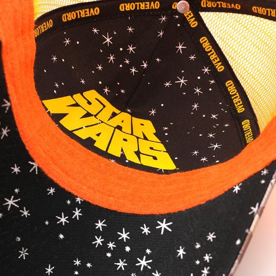 Underside of the Droopy McCool trucker cap showing a starry black brim print with yellow Star Wars logo, orange trim, yellow mesh crown, and yellow Overlord taping.