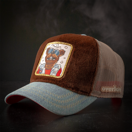 Dark brown faux fur trucker cap with acid washed blue denim brim and khaki mesh featuring a woven patch of Chuck the Stoat from Emmet Otter attached to the crown.