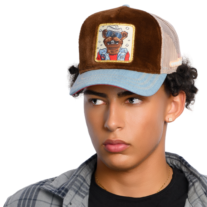 Man wearing dark brown faux fur trucker cap with acid washed blue denim brim and khaki mesh featuring a woven patch of Chuck the Stoat from Emmet Otter attached to the crown.