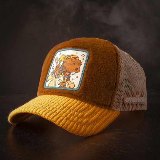 Charlie Muskrat from Emmet Otter patch on a brown fuzzy-textured retro trucker cap with a blue-bordered patch, yellow ribbed-texture brim, and dark mesh sides.