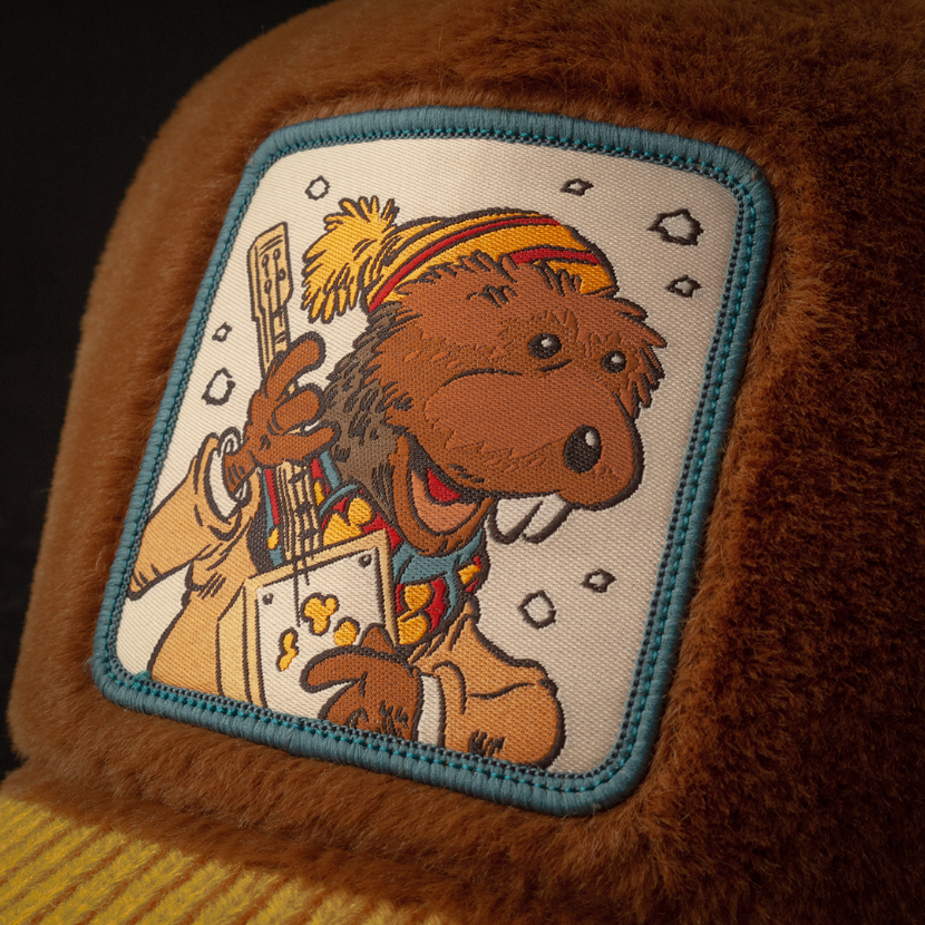 Woven patch of Charlie Muskrat from Emmet Otter playing a washtub guitar, blue-bordered on a brown fuzzy-textured retro trucker cap.