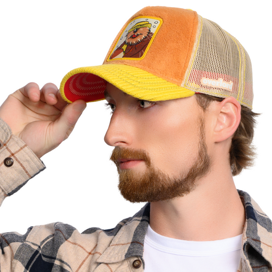 Man wearing brown faux fur trucker cap with yellow sweater knit brim and khaki mesh featuring a woven patch of Wendell the Porcupine from Emmet Otter attached to the crown.