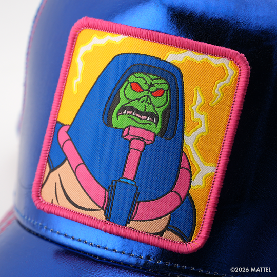 Woven patch of Man-E-Faces from Masters of the Universe with a green skull face in a blue helmet, set against a yellow lightning background with pink border, stitched onto the metallic blue retro trucker cap.