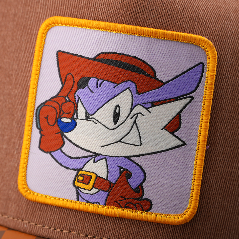 Woven patch of Fang from Sonic the Hedgehog wearing a red hat and pointing upward, set against a light purple background with gold border, stitched onto the brown retro trucker cap.