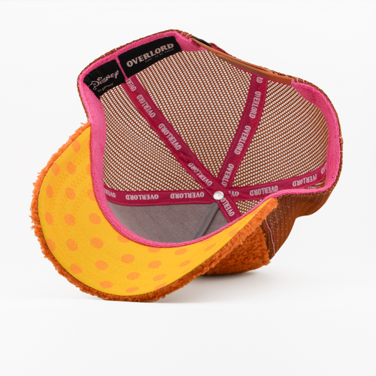 Underside of the Fozzie Bear retro trucker cap, showing a yellow polka-dot brim, a Disney tag, tan mesh crown, and pink Overlord branded taping with white text.
