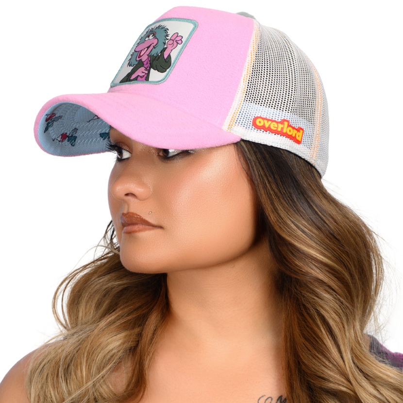 Woman wearing purple fleece trucker cap hat with Fraggle Rock Mokey woven patch against white background