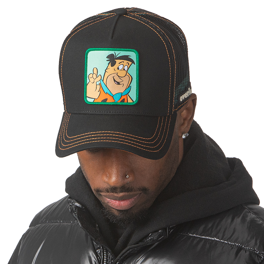 Man wearing black OVERLORD X Flintstones Fred Flintstone trucker baseball cap with orange stitching. PVC Overlord logo.