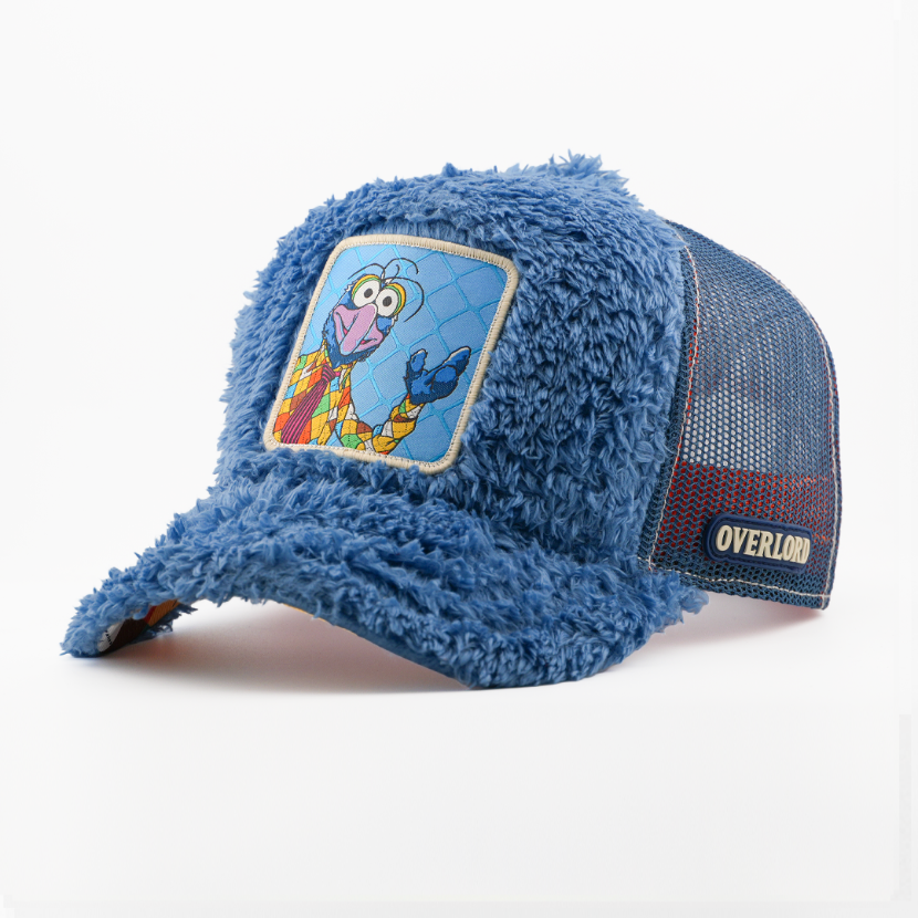 Fuzzy-textured blue retro trucker cap with a patch of Gonzo from The Muppets in a colorful patterned suit on a lattice-pattern blue background, blue mesh back with tan Overlord logo.