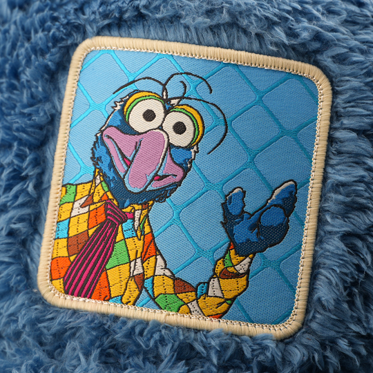 Close-up of a woven patch showing Gonzo from The Muppets in a colorful argyle-pattern outfit on a lattice-pattern blue background, stitched onto fuzzy-textured blue fabric with a tan border.