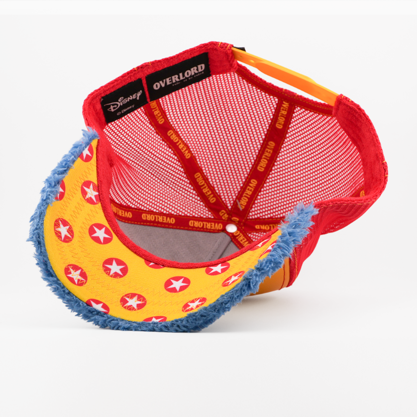 Underside of the Gonzo retro trucker cap, showing a yellow star-print brim, a Disney tag, red mesh crown, and red Overlord branded taping with orange text.