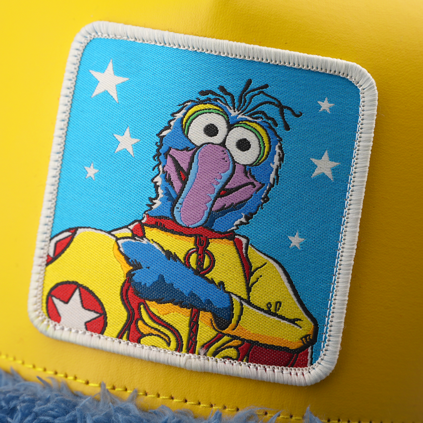 Close-up of a woven patch showing Gonzo from The Muppets in a yellow superhero costume with a red star emblem on a star-print blue background, stitched onto yellow fabric with a white border.