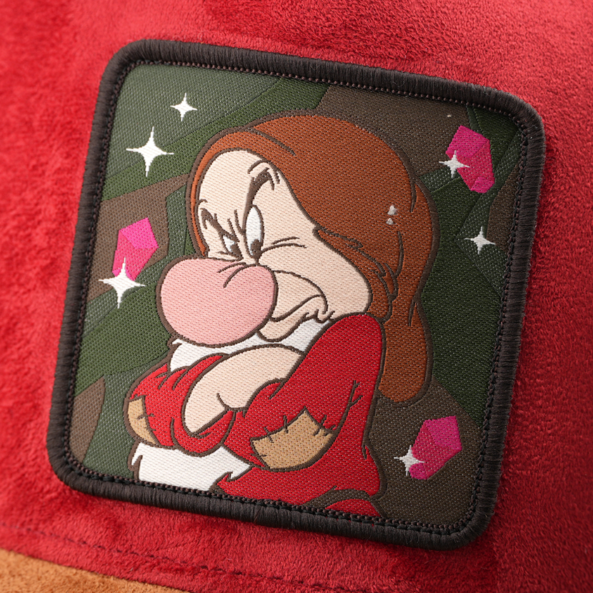 Woven patch of Grumpy from Disney's Snow White and the Seven Dwarfs frowning with arms crossed against a mine and gem-themed background, with a black border, stitched onto the red suede-textured retro trucker cap.