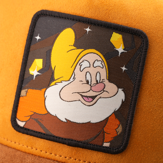 Woven patch of Happy from Disney's Snow White and the Seven Dwarfs smiling against a mine and gem-themed background, with a black border, stitched onto the orange suede-textured retro trucker cap.