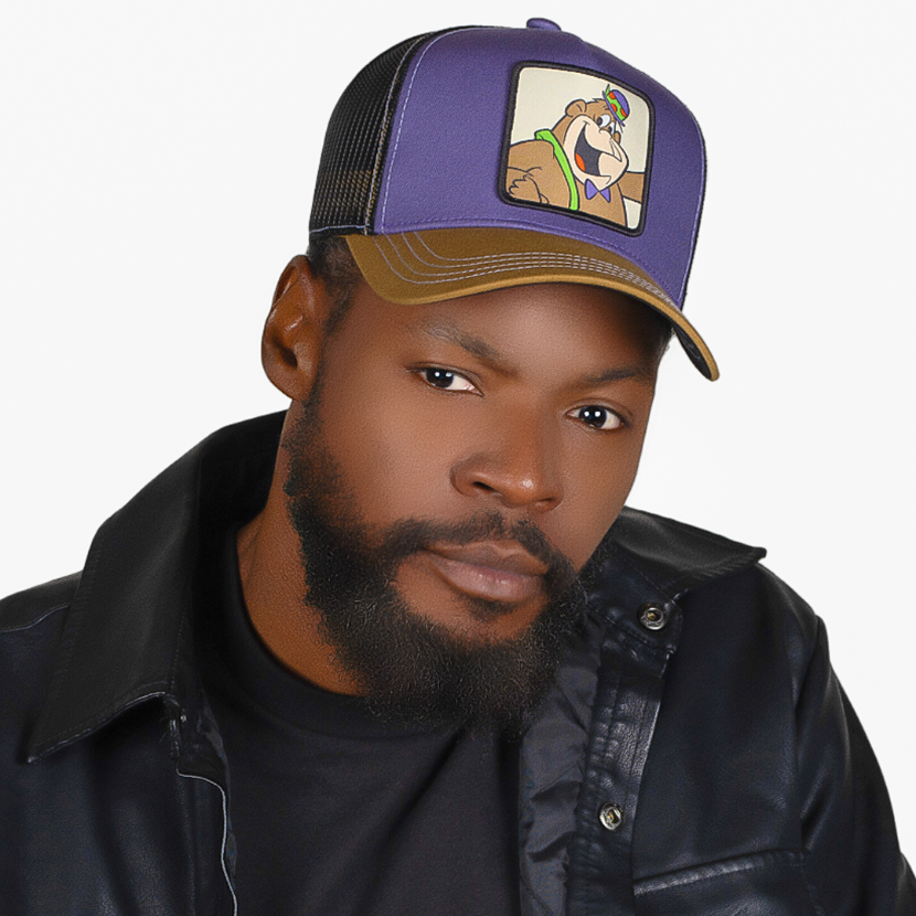 Man wearing brown and purple twill trucker cap with black mesh featuring a woven patch of Magilla Gorilla from the classic Hanna-Barbera cartoons attached to the crown.