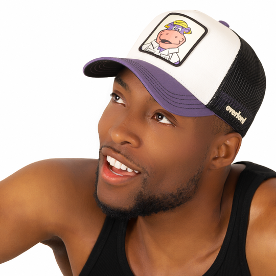 Man wearing white and purple twill trucker cap with black mesh featuring a woven patch of Peter Potamus from the classic Hanna-Barbera cartoons attached to the crown.