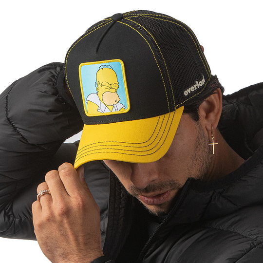 Man wearing black and yellow OVERLORD X The Simpsons Homer Doh trucker baseball cap hat with black stitching. PVC Overlord logo.