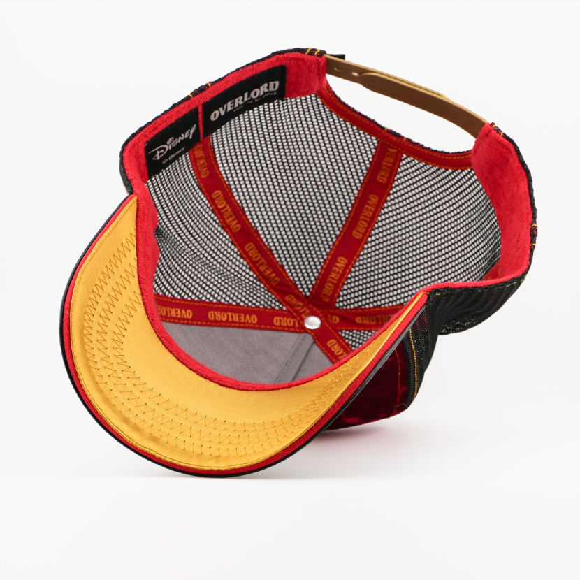Underside of the Jafar retro trucker cap showing a gold brim, Disney tag, black mesh crown, and red Overlord taping.