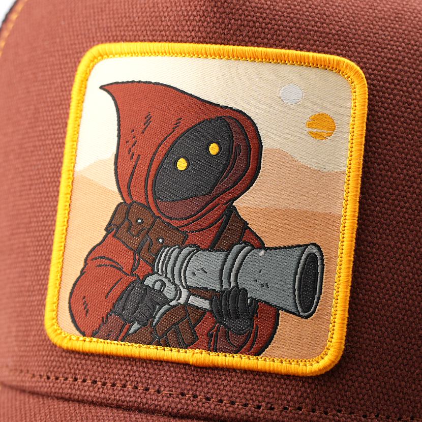 Close-up of a woven Jawa from Star Wars patch wielding a blaster, stitched onto rust-brown trucker cap fabric.