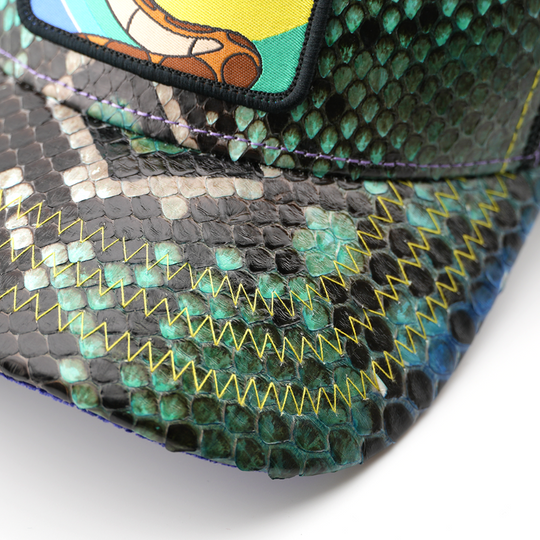 Close-up of the green snakeskin-textured brim on the Kaa from Disney's The Jungle Book retro trucker cap, showing yellow zigzag stitching and the edge of the woven patch.