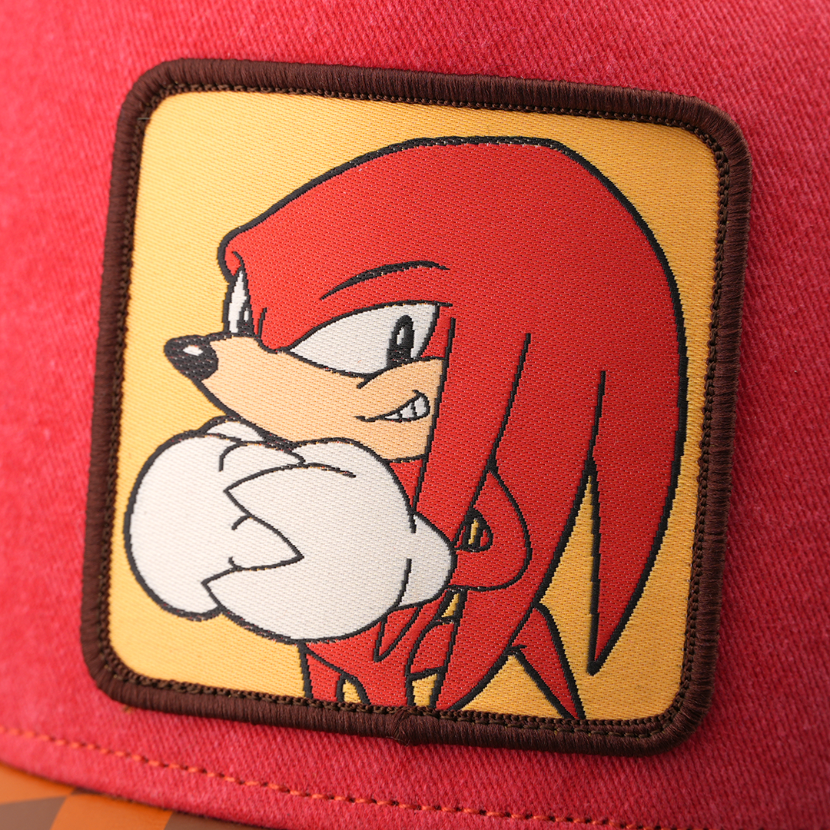 Woven patch of Knuckles from Sonic the Hedgehog with clenched fists, set against a tan background with dark brown border, stitched onto the red retro trucker cap.