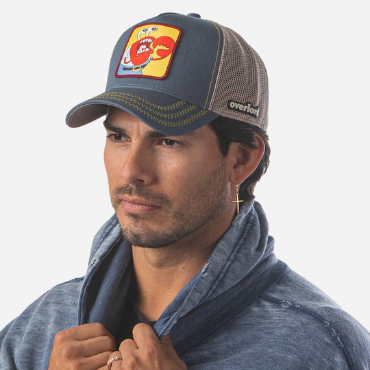 Man wearing steel blue OVERLORD X SpongeBob choking Krusty Krab trucker baseball cap hat with yellow zig zag stitching. PVC Overlord logo.