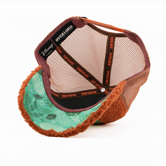 Underside of the Lost Boy Cubby retro trucker cap, showing a green leaf-print brim, a Disney tag, brown mesh crown, and brown Overlord branded taping with orange text.