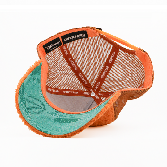 Underside of the Lost Boy Slightly retro trucker cap, showing a teal fern-print brim, a Disney tag, gray mesh crown, and orange Overlord branded taping with white text.