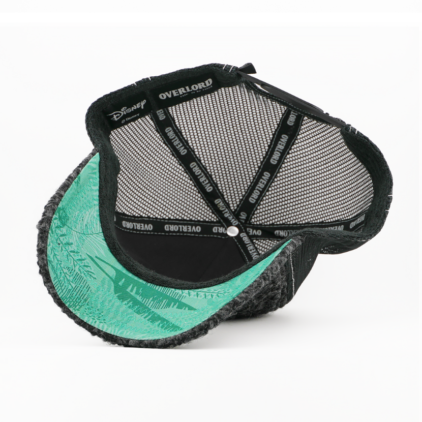 Underside of the Lost Boy Snootles from Disney's Peter Pan retro trucker cap, showing a teal fern-print brim, a Disney tag, black mesh crown, and black Overlord branded taping with white text.