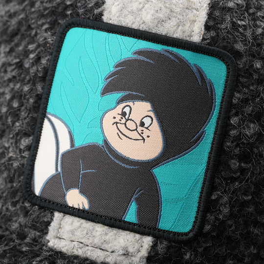 Close-up of a woven patch showing Lost Boy Snootles from Disney's Peter Pan smiling on a teal background, stitched onto boucle-textured charcoal fabric with a black border.