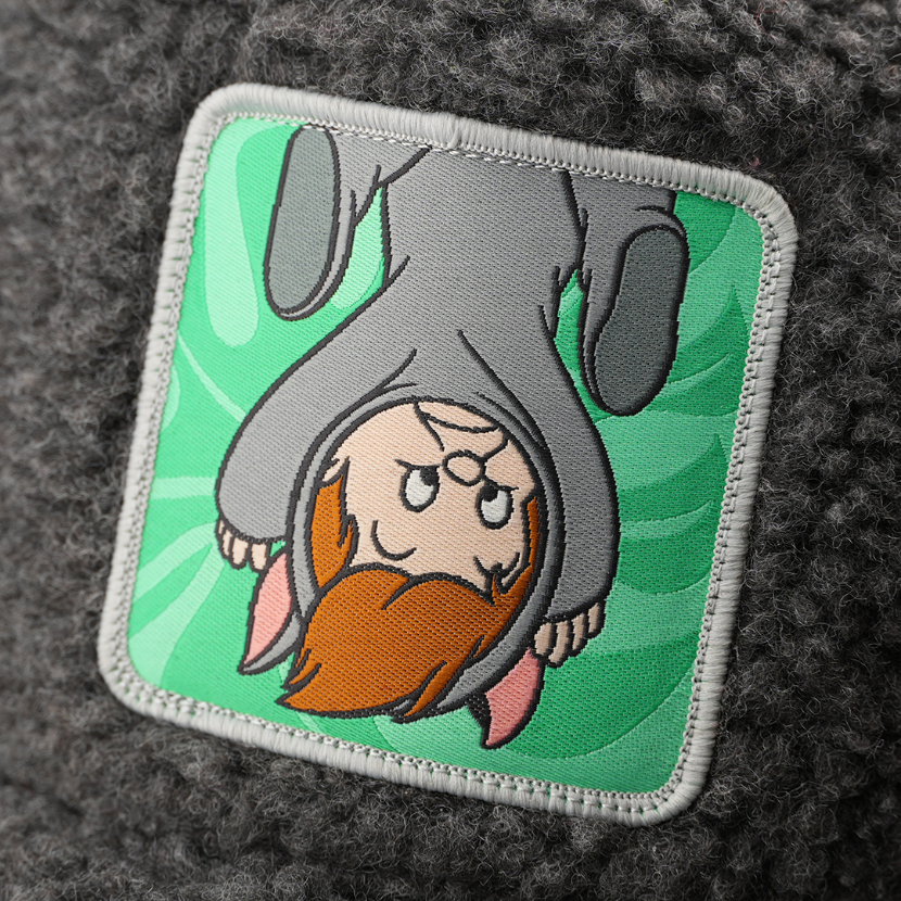 Woven patch of the Second Twin from Disney's Peter Pan hanging upside down in an animal costume against a leafy background, with a gray border, stitched onto the charcoal boucle-textured retro trucker cap.