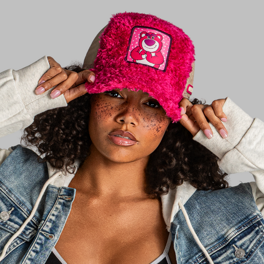 Person wearing a pink fuzzy beanie with a cartoon character patch, holding it on their head.