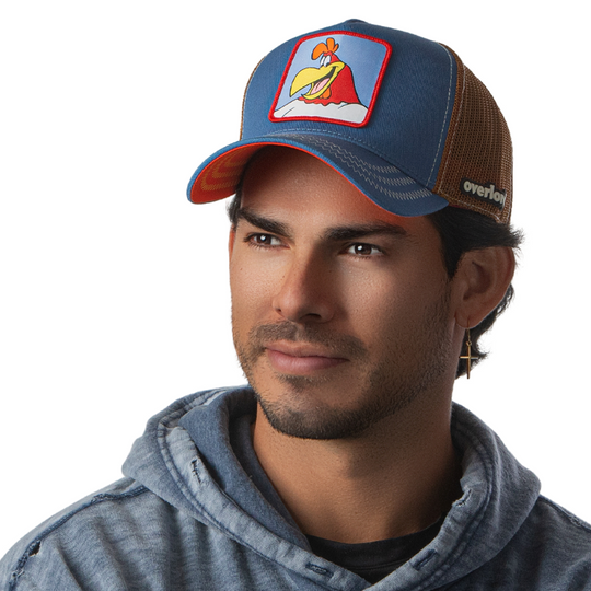 Man wearing a steel blue twill trucker cap with brown mesh featuring a woven patch of Foghorn Leghorn from Looney Tunes attached to the crown.