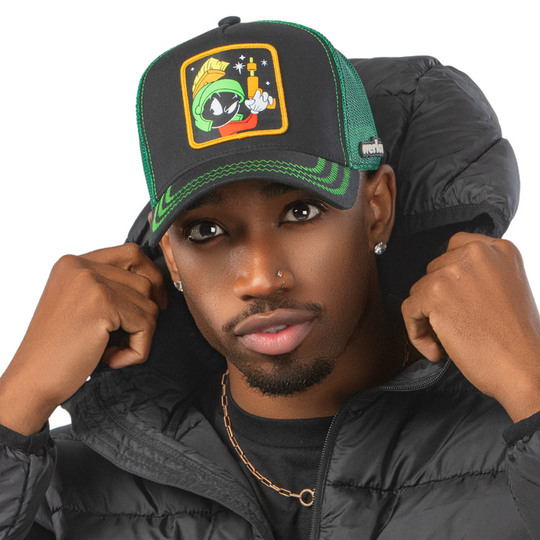 Man wearing black OVERLORD X Looney Tunes Marvin the Martian holding a laser gun trucker baseball cap hat with green zig zag stitching. PVC Overlord logo.