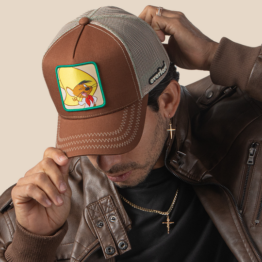 Man wearing brown OVERLORD X Looney Tunes Speedy Gonzales trucker baseball cap hat with khaki zig zag stitching. PVC Overlord logo.