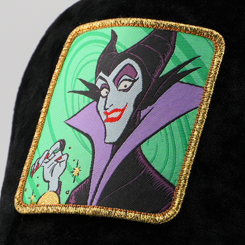 Close-up of the Maleficent from Disney's Sleeping Beauty patch with glowing hand against a swirling green background, stitched onto the black velvet retro trucker cap fabric with gold border.